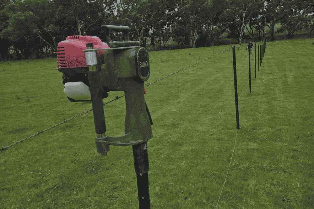 Post driver sitting on top of a star picket along a wire fence line in a green rural paddock-